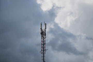 Obraz premium Cell tower with mobile antennas against dramatic cloudy sky providing wireless communication network signal in rural area
