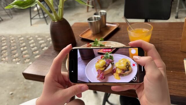 Man making vertical video, stories, photo for social media of delicious restaurant food on smartphone. Male influencer shoot clip, film, reels on phone camera of eggs benedict breakfast.