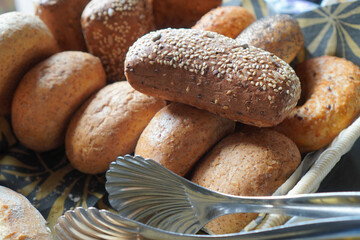 Close-up of brown and white bread buns in buffet setting with metal tongs.