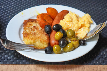 Person serving scrambled eggs and sausage onto plate from buffet counter.