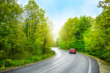 Red car driving on the panoramic road landscape in summer. Nature landscape on highway for summer vacation travel. Forest road scene on beautiful nature panorama trip in Europe. Car drive on mountain.