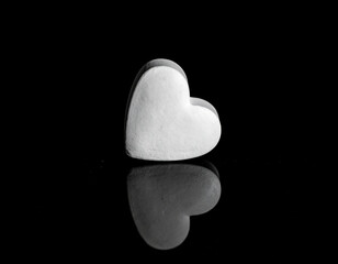 A single, matte white heart is sharply contrasted against a deep black reflective surface in a monochromatic composition, emphasizing shape, shadow, and a sense of profound emotion or concept.
