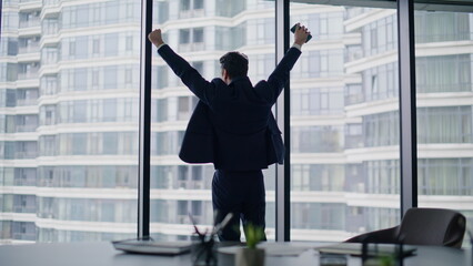 Business owner enjoying success raising hands in office. Successful businessman