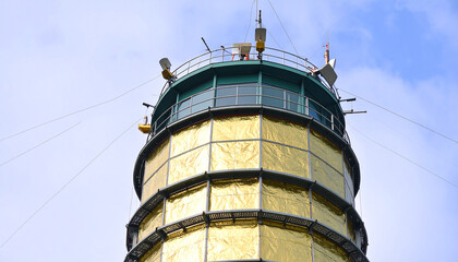Naklejka premium Golden Tower Ascending: An imposing tower of shining gold rises against a bright sky, its architecture echoing both classic design and modern purpose. The pinnacle of ingenuity.