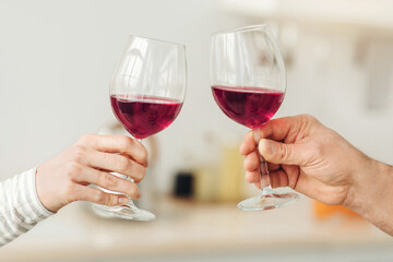 Romantic couple enjoying dinner at home, love, relationship and love concept. Happy couple celebrating and holding glasses of red wine in modern kitchen interior, close up, copy space, cropped