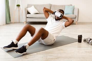 Naklejka premium Virtual Workout. Fit Black Guy Wearing VR Headset Doing Abs Exercise On Floor At Home. Augmented Reality Technology And Sport, Futuristic Training And Smart Fitness Concept