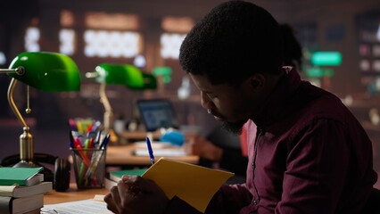 African american guy studies for a critical law exam and reading specialty books to complete class notes with reliable academic information. Studying in the library before the test. Camera A.
