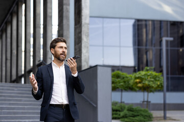 A professional male dressed in formal attire communicates using his smartphone outside a modern building, depicting business activities and communication in an urban setting.