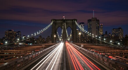 Fototapeta premium Night view of the Brooklyn Bridge in New York City, with city lights and blurred car trails on the roadway.