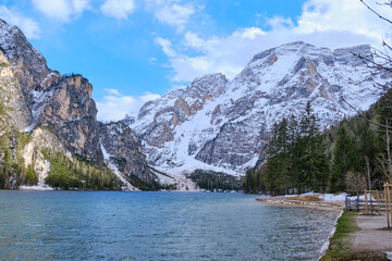 Obraz premium March 2025: view of Braies Lake in winter, with a frozen surface marked by trails, surrounded by snow covered cliffs, rugged rocks, and evergreen trees.a