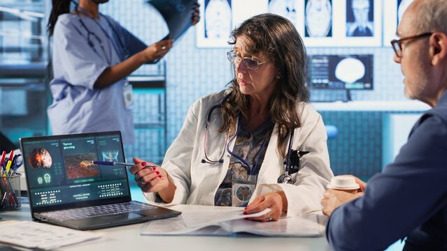 Female radiologist examines a tumor scan with male patient, providing medical diagnosis and discussing immunotherapy, chemotherapy, and lifestyle changes for better health. Camera B.