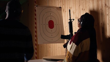 Shooting gallery client using rifle to hit targets, getting congratulated by instructor after great...