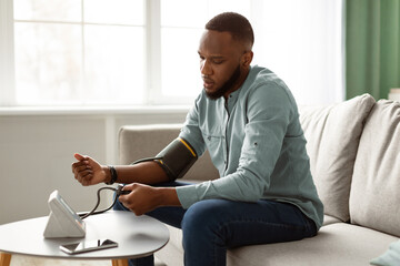 Hypertension Problem. Black Young Man Measuring Arterial Pressure Feeling Bad Sitting On Couch At...