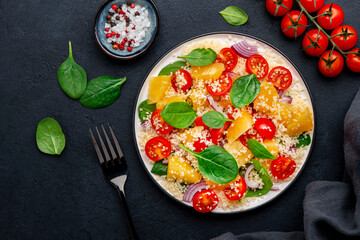 Gourmet vegan salad with couscous, tomatoes, onion, spinach and orange. Black background, top view