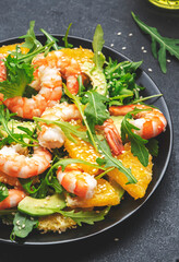 Seafood salad with shrimps, avocado, juicy orange, fresh arugula and sesame on black table, top view