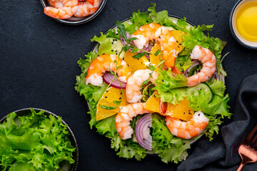 Juicy shrimp salad with orange, lettuce, red onion with olive oil and juice dressing, black background, top view