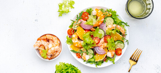 Fresh shrimp salad with orange, lettuce, tomatoes, cucumbers, onions and sesame seeds with olive oil, white background, top view