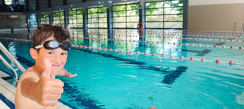 Happy boy giving a thumbs up in an indoor swimming pool. Concept of self-confidence in children's swimming lessons, child development, children's sports.
