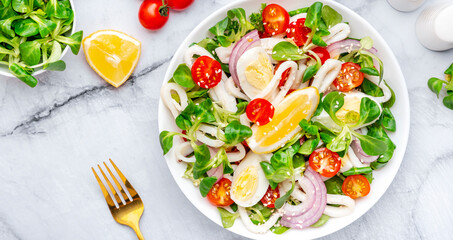 Seafood salad with squid, orange, tomatoes, lamb lettuce and olive oil with lemon juice dressing, gray table background, top view