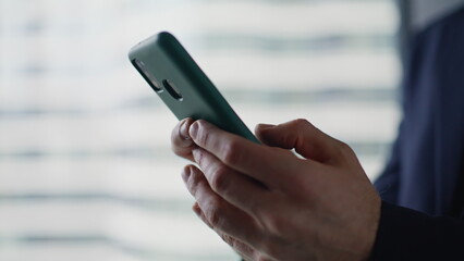 Businessman hands texting mobile phone in light office interior closeup. 