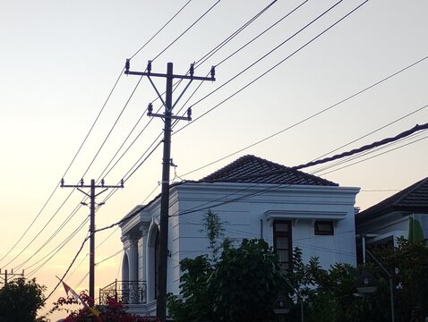 Urban sunset view with power lines and tropical house in Indonesia, peaceful residential area silhouette.
