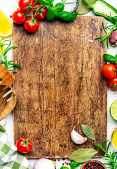 Healthy cooking food background with spices, herbs, kitchen utensils on wooden cutting board, top view. Peppercorn, garlic, basil, lemon, tomatoes and other ingredients