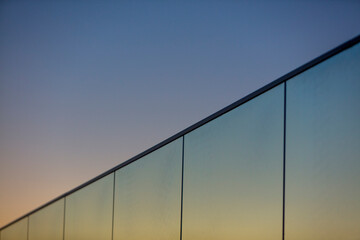 A glass balustrade with a blue and orange sky at sunset. A glass balustrade with an aluminum profile under the open sky on a warm day. Glass panels on a balcony or terrace.