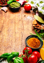 Healthy cooking and food background with spices, herbs, curry and kitchen utensils on wooden cutting board, top view. Peppercorn, garlic, basil, lemon, tomatoes and other ingredients