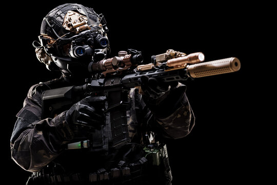 Professional soldier in tactical gear aiming a rifle in low light