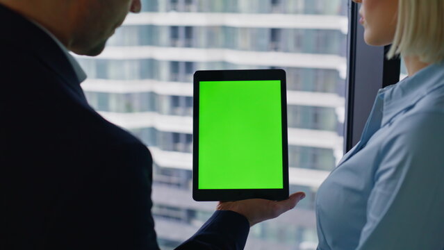 Coworker tapping green screen tablet showing data to businesswoman closeup.