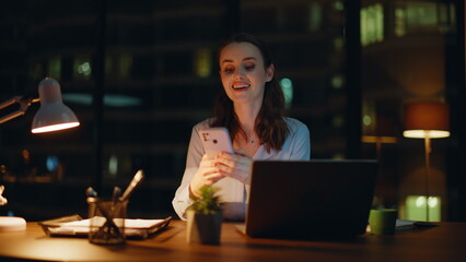 Smiling woman texting smartphone at night office closeup. Happy lady freelancer