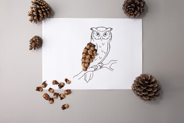DIY owl collage with pine cone parts and drawing on grey surface, great for art education, children books, nature activities, craft stores, seasonal ads, and learning platforms,