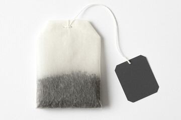 A single teabag with a black tag on a white background ready for brewing a warm cup of tea beverage