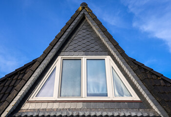 Triangular dormer window with slate roof tiles against blue sky
