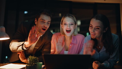 Friendly colleagues greeting webcam laptop sitting at night office closeup.