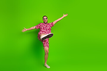 Happy young man in vibrant pink leopard print outfit posing against bright green background with expressive gestures