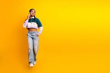 Fototapeta premium Cheerful young woman with braided hair talking on phone and posing confidently against a vibrant yellow background