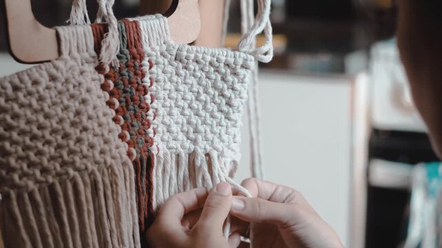 Close-up of macrame weaving with a woman hands working on a colorful fiber pattern