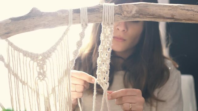 Soft glowing scene of a Caucasian woman weaving macrame fibers by a window