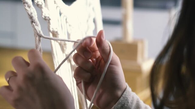Neutral toned portrait of a Caucasian model tying intricate macrame knots on a driftwood frame