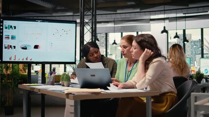 Businesswomen compare analytics and plan strategy in a modern workspace, supporting development vision together. Diverse associates collaborating and reviewing data analytics. Camera A. - Powered by Adobe