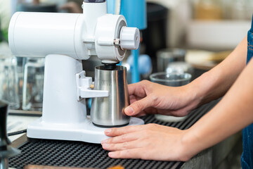 Small business entrepreneur coffee shop cafe. Asian woman barista using coffee grinder grinding roasted coffee beans making brewed coffee on counter bar. Waitress serving beverage drink to customer.