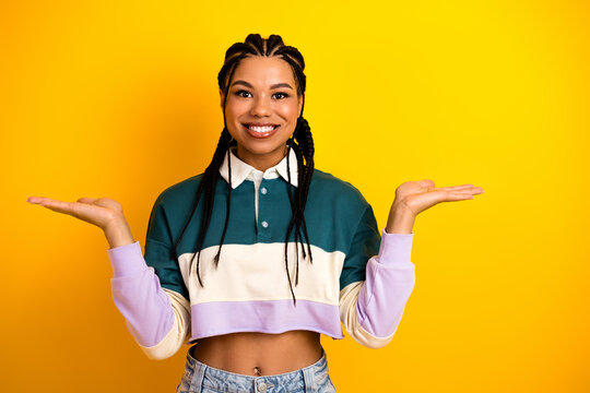 Cheerful young woman in colorful casual outfit presenting with her hands against a vibrant yellow background - Powered by Adobe