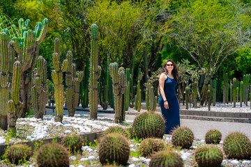 Happy smiling young Latina woman wearing a sleek navy blue dress and sunglasses strolls confidently through the cactus-filled paths of Chapultepec Botanical Garden, a lush space in Mexico City