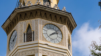 Architectural clock tower with Mudejar decoration, seen from a low angle on a clear day with blue sky.