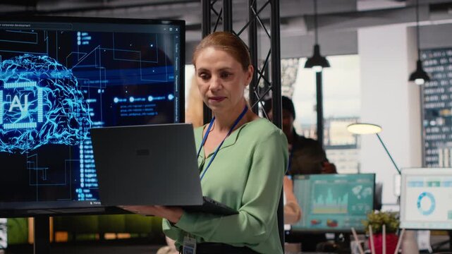 Female entrepreneur works with neural networks for analytics, looking at AI automation algorithms on big monitor. Artificial intelligence helps decision making in a corporate setting. Camera B.
