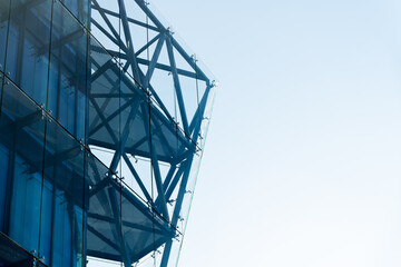Contemporary glass facade with visible steel framework and geometric lines against a clear sky. Suitable for illustrating architecture, construction, or urban development concepts.