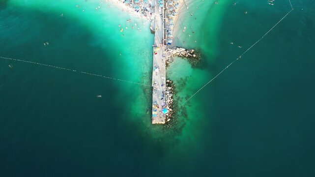 Drone view of a concrete pier stretching into turquoise Adriatic waters