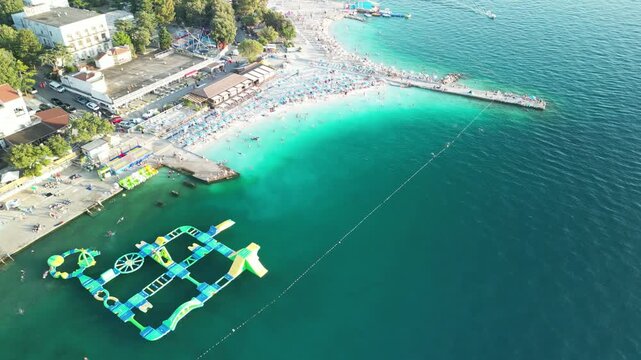 Drone view of Selce Beach in Croatia showing a floating water park, sunbathers, and turquoise waters