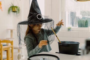 Cute girl in a witch's hat having fun cooking Halloween pasta.